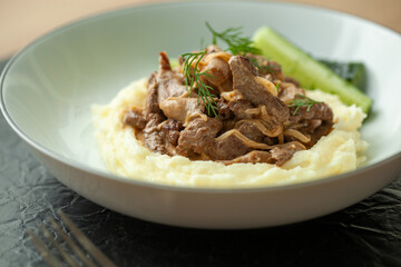 Delicious beef stroganoff served on creamy mashed potatoes with tangy pickles and fresh dill, a comforting russian dish