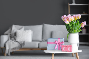 Calendar with date of International Women's Day, tulips and gift box on table in living room, closeup