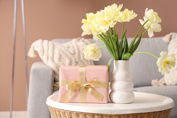 Vase with flowers and gift box on coffee table in living room