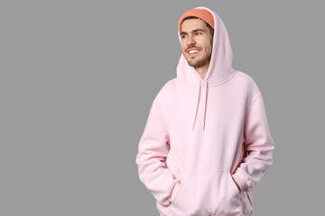 Handsome smiling young man in stylish pink hoodie and peach hat posing on grey background