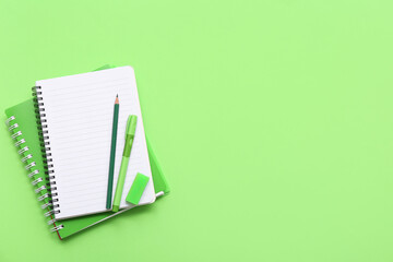 Notebook with pencil and pen on green background. Top view