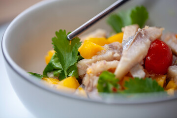Picking fresh cilantro with metal chopsticks from a bowl of ceviche with mango and cherry tomatoes, a colorful seafood dish perfect for a gourmet meal or appetizer