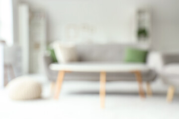 Blurred view of light living room with grey sofa and coffee table
