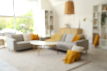 Blurred view of light living room with grey sofas, table and shelf units