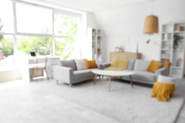 Blurred view of light living room with grey sofas, table and shelf units