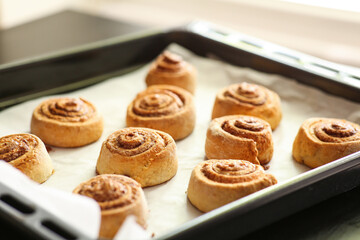 Baking tray with tasty cinnamon rolls on table in kitchen