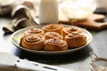 Plate with tasty baked cinnamon rolls on table in kitchen