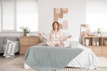 Young woman with headphones and laptop meditating in bedroom