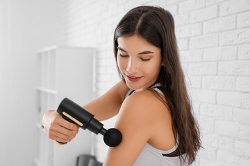 Sporty young woman using percussive massage device after training in gym