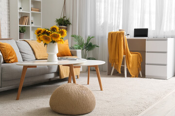 Comfortable sofa, coffee table with sunflowers and workplace in interior of living room