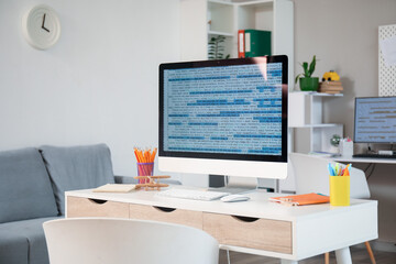 Computer monitor with code and stationery on programmer's desk in office