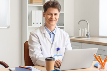 Male medical intern studying with laptop at table in clinic