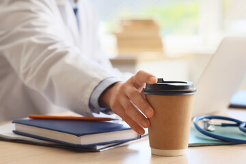 Male medical intern taking cup of coffee from table in clinic, closeup