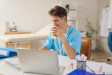 Male medical intern with coffee cup studying at table in clinic