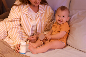 Mother with bottle of milk and her little baby in bedroom at night, closeup