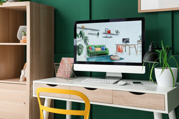 Interior designer's workplace with computer and plant near green wall in office