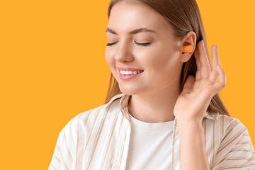 Young woman with ear plug on yellow background, closeup