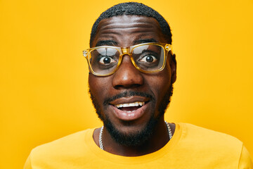 Smiling young man wearing stylish yellow glasses, cheerful expression on a vibrant yellow background, showcasing joy and enthusiasm in a contemporary casual outfit