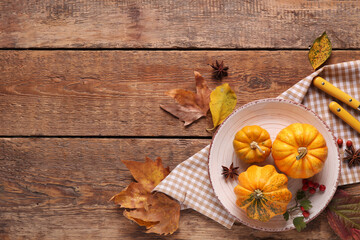 Plate with fresh pumpkins, star anise, rose hip berries and autumn leaves on wooden background