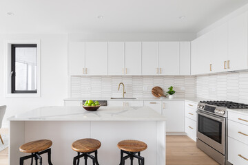 A beautiful kitchen detail with white cabinets, a gold faucet, white marble countertops, and a brown picket ceramic tile backsplash. No brands or labels.