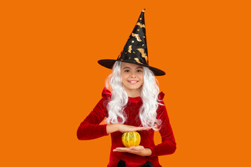 Halloween pumpkin in hand of teen girl wearing All Hallows party holiday costume of witch hat isolated on orange