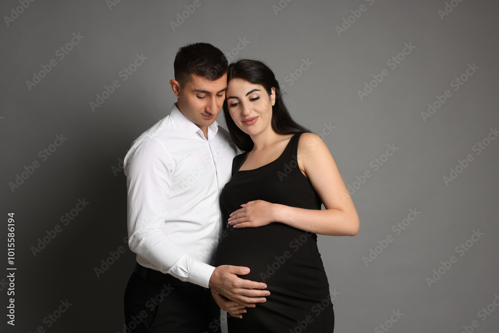 Wall mural Beautiful pregnant woman with her husband on grey background