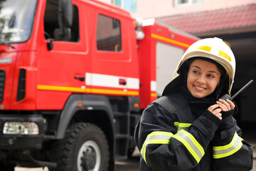 Firefighter in uniform with portable radio set near fire truck outdoors