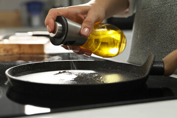 Woman pouring oil into frying pan on cooktop in kitchen, closeup