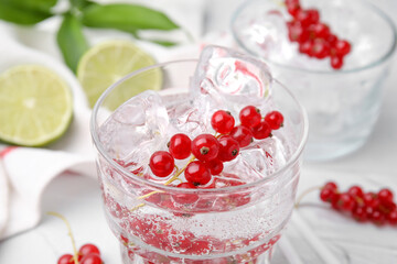 Refreshing water with red currants in glass on light table, closeup