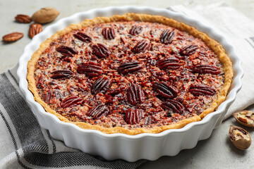 Delicious pecan pie in baking dish and fresh nuts on gray textured table, closeup