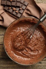 Chocolate dough in bowl and whisk on wooden table, top view