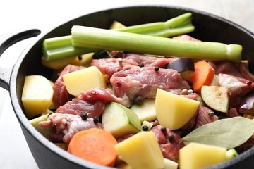 Cooking stew. Uncooked meat and vegetables in pot on white tiled table, closeup