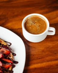 Taza con café americano y un plato con waffle de fresa