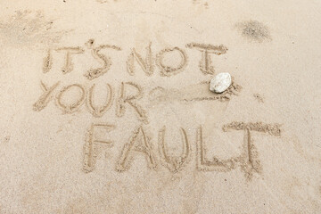 Motivation quotes It is not Your Fault written in the sand of the beach