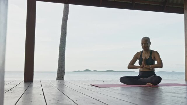 Senior Woman Practicing Yoga by the Ocean in Wooden Gazebo, Folding Hands in Lotus Pose, Healthy Lifestyle