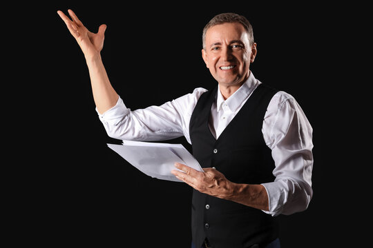 Mature actor reading film script on dark background