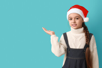 Cute little girl in Santa hat showing something on blue background