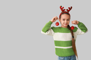 Cute little girl in reindeer horns with Christmas balls on grey background