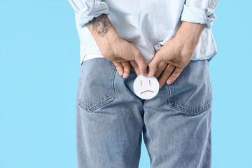 Young man with hemorrhoids and sad smile on blue background, back view