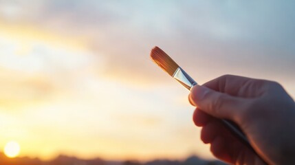 A person grips a paintbrush firmly, poised to unleash creativity outdoors. The background features a soft light sky, capturing an inspiring moment
