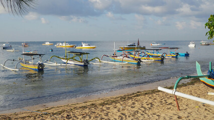 Wooden Fishing boats parked on the beach of Sanur Bali on blue sky background.