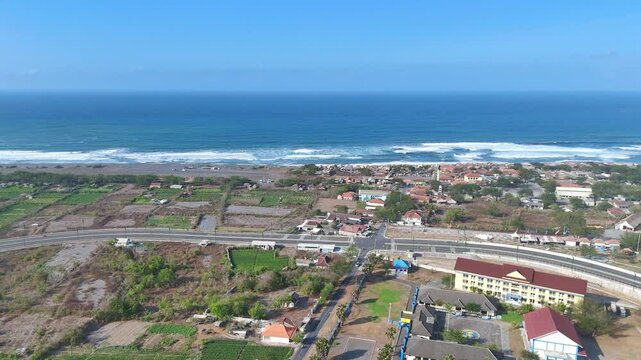 Aerial view of blue ocean water with a long silky brown sand and blue sky at Depok Beach, Indonesia. 4K drone footage of tropical beach.