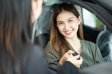 Saleswoman giving car key of new car to smiling female customer at showroom