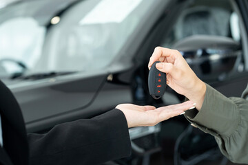 Close Up Of Saleswoman giving car key of new car to Businesswoman at showroom