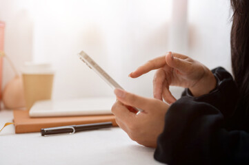 A close-up of a woman in a black sweater using her smartphone while sitting at a table indoors.