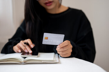A cropped image of a woman using her phone and holding a credit card while planning her finances.