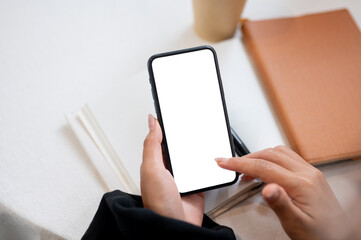 A close-up of a woman's hand holding a smartphone with a white screen mockup over a table.