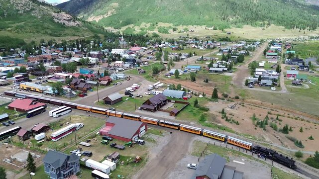 Aerial flyover shot of historic downtown Silverton, Colorado. Flight shows a scenic train preparing for departure and the northeast side of the town with mountains in the background.