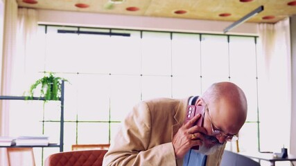 Indian Asian elderly businessman with a beard and suit, with documents in hand, sitting in a revolving chair while discussing important business matters on the phone 