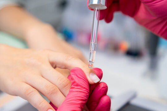 Manicurist applying an oil for cuticulas removing from the nail during manicure session